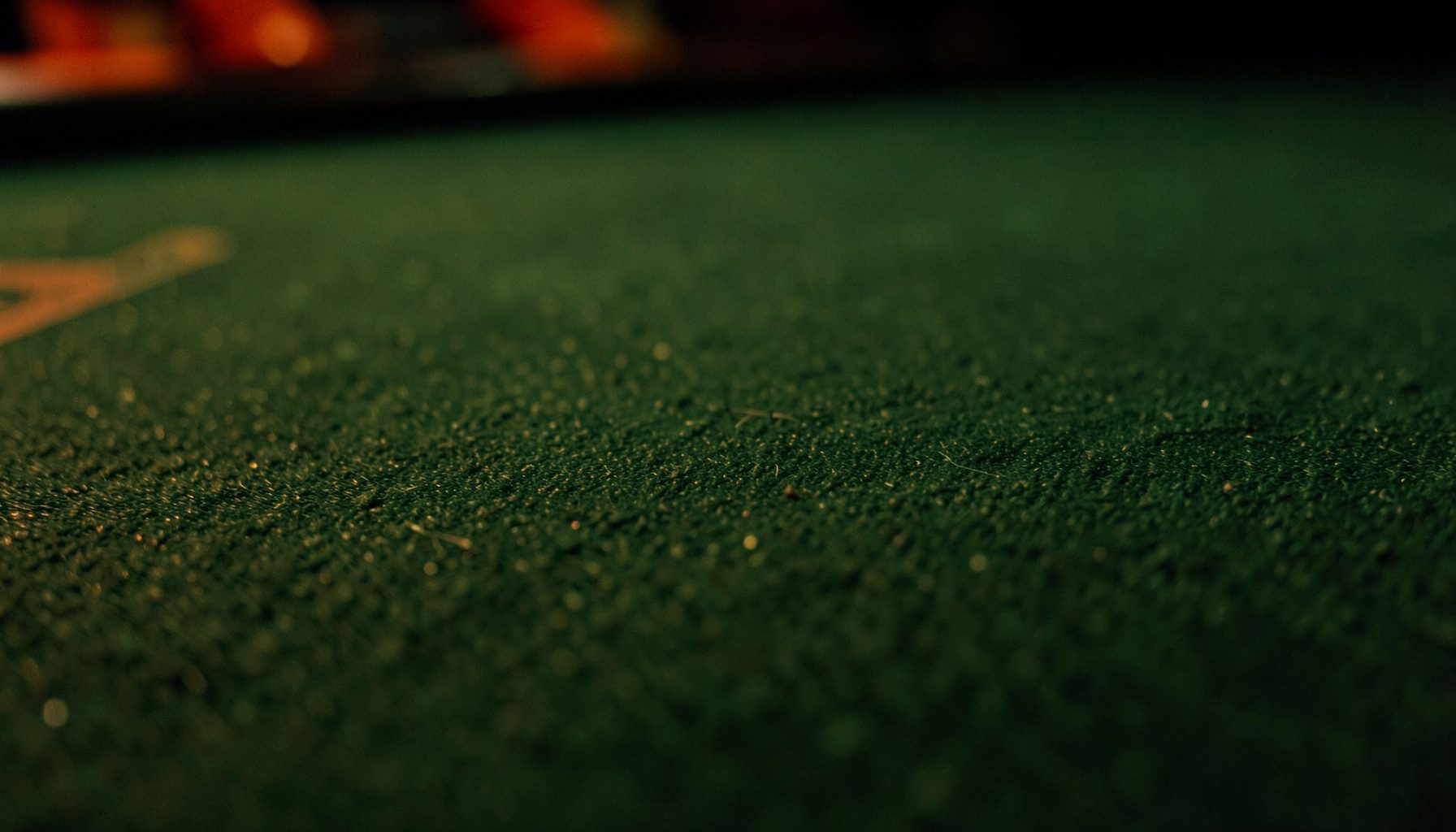 Dark atmospheric close-up of a green felt casino table surface with subtle texture and soft ambient lighting